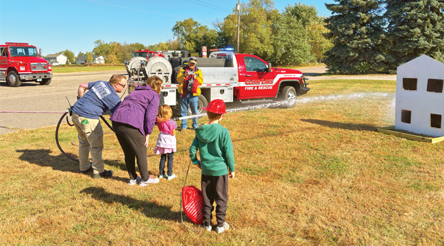 Lt. Brandon Weis, grandparents Greg and Brenda Mass, and brother Easton watch Adaline spray the hose. (Patriot Photo by Don Bellach)