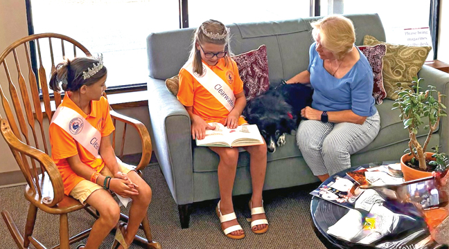 CLEARWATER HERITAGE FESTIVAL PRINCESSES CHARLENE AND ALEXIS read to Maggie Mae, the library’s visiting therapy dog during the Heritage Festival at the beginning of August. (Submitted Photo).