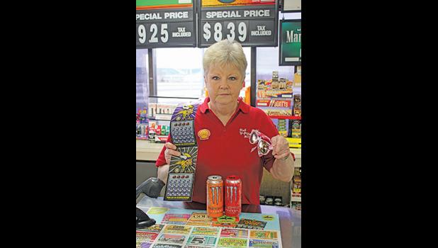 RENE BAUMGARTNER, a four-year employee at Deli Plus, shows some of the super items that would make great Christmas presents or stocking stuffers such as lottery ticket, sunglasses, scratch-offs and Monster drinks. (Photo by Bill Morgan). 