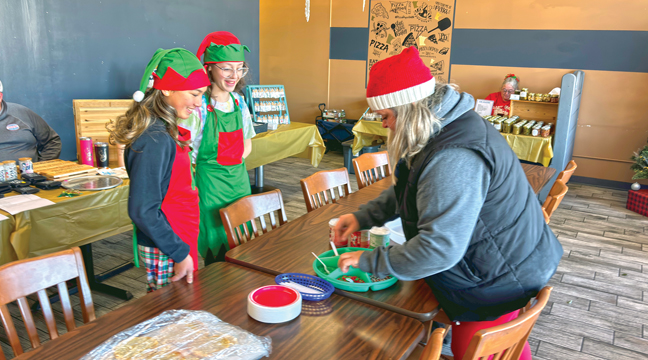 Owner Morgan duMonceaux(R) gets elves Myla and Arya ready to help kids decorate ornaments and cookies. (Patriot photo by Don Bellach)
