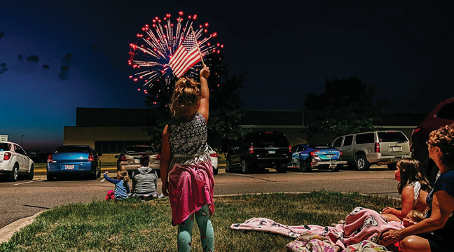 Aurora Winkelman waved her USA Flag at Thursday’s Firework show in Big Lake. Hundreds showed up in parking lots and along streets to get a glimpse of the spectacle on a warm summer night. (Photo by Jayme Winkelman). See Shelley Berthiuame’s story below for how others celebrated Independence Day in Big Lake.