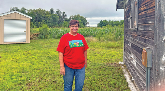 Farm Friends Barn organizer Jean Johnson is pictured between the granary building and the new storage shed that will be used to store tools for the community gardens.  Behind Johnson is the area that will be used for the gardens in 2026. (Patriot Photo by Mark Kolbinger.)
