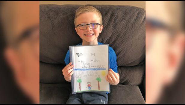 FIRST-GRADER CROSBY SPEAR proudly holds his book he wrote and illustrated, talking of how he misses school. (Submitted Photos)