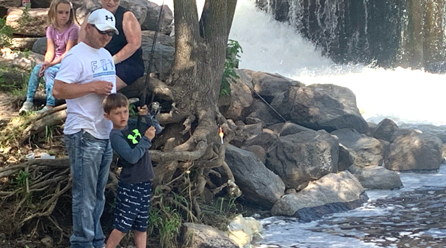 HUNTER REMER works to bring in his fish while his dad Ryan Remer, grandma Becky Himmelspach, and friend Maevyn Geyer cheer him on. (Photo by Penny Leuthard.)