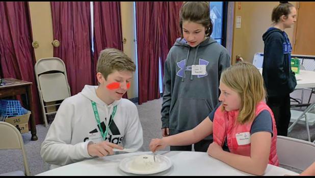 (L) Caden Elliot, 10th grader from Becker, Benton County 4-H Ambassador showing participants (Center) Chloe Bechtold and (R) Delayna Rife how to play the flour game at the 4-H Glow Lock-In.