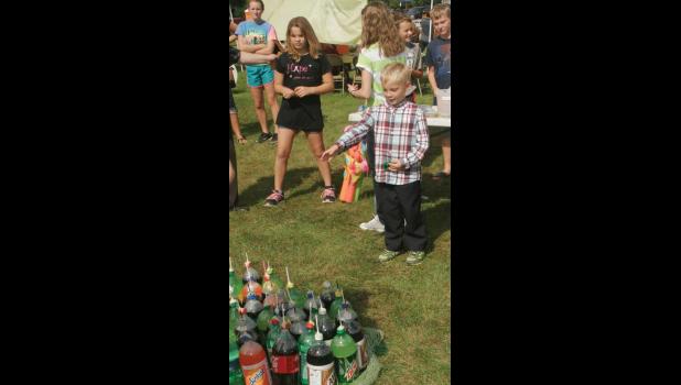Nicholas is playing ring toss and trying to win a two liter of soda at the block party.