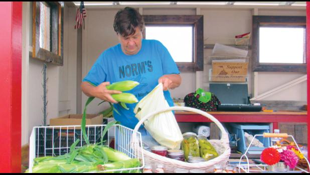 LONG TIME FARMER’S MARKET vender Jean Johnson of Norm’s Farm Market bags up a customer’s fresh sweet corn purchase. (Photo by Penny Leuthard)