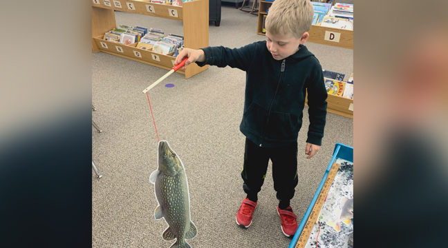AARON BECK catches a huge northern pike at the Headwaters exhibit at the Clearwater Library. (Photo by Penny Leuthard.)