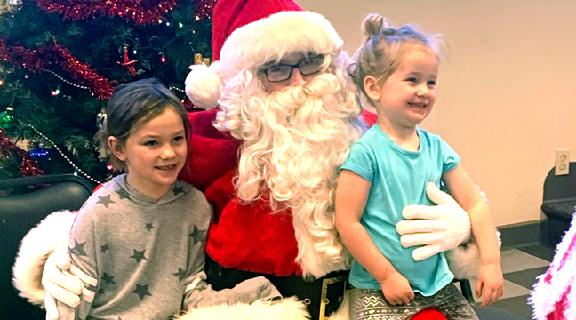 THREE-YEAR-OLD RAEGAN PICHOTTA beamed from Santa’s lap as she and her sister Morgan sat for their picture. (Photo by Penny Leuthard.)