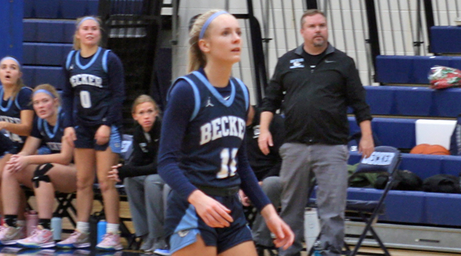 Becker’s Adeline Kent gets ready to retreat on defense after a Bulldog bucket in the paint as Head Coach Dan Baird watches in the background.  Kent led Becker with 21 points in just 24 minutes of action. (Photo by Mark Kolbinger.)