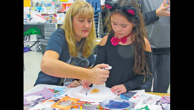 THIRD-GRADE TEACHER AND VOLUNTEER DANNA GOHMANN helps Jade D. with her nature painting during Clearview’s family forest night.